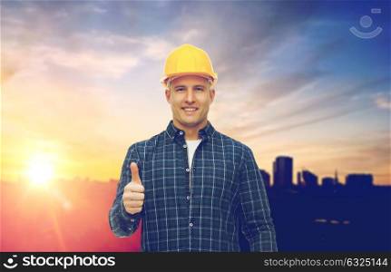 construction, building and gesture concept - smiling male builder or manual worker in yellow hard hat showing thumbs up over city background. male builder in yellow hard hat showing thumbs up