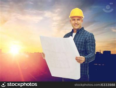 construction, building and people concept - male builder in yellow hard hat with blueprint over city background. male builder in yellow hard hat with blueprint
