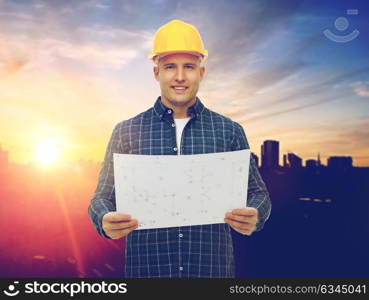 construction, building and people concept - male builder in yellow hard hat with blueprint over city background. male builder in yellow hard hat with blueprint