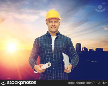 construction, building and people concept - male builder or foreman in yellow hard hat with blueprint and clipboard over city background. builder in hard hat with blueprint and clipboard