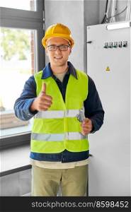 construction business and building concept - happy smiling male electrician or worker in helmet and safety west with papers on clipboard and pencil at electric board. electrician with clipboard at electric board