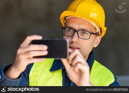 construction business and building concept - male builder in helmet and safety west taking picture with smartphone. male builder taking picture with smartphone