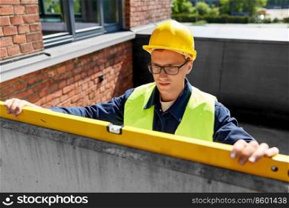 construction business and building concept - male builder with level measuring wall. male builder with level measuring wall