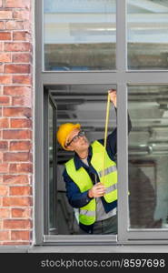 construction business and building concept - male builder with ruler measuring window. male builder with ruler measuring window