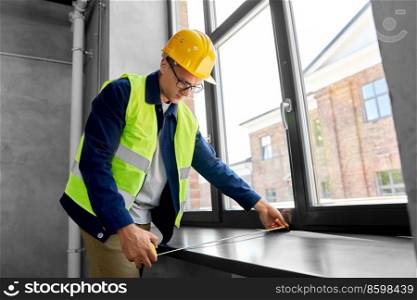construction business and building concept - male builder with ruler measuring window sill. male builder with ruler measuring window sill