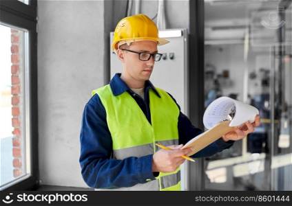 construction business and building concept - male electrician or worker in helmet and safety west with papers on clipboard and pencil at electric board. electrician with clipboard at electric board