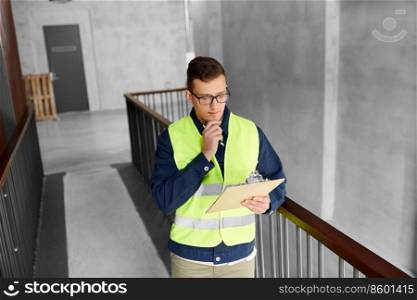 construction business and building concept - male worker in safety west with clipboard working at office. male worker with clipboard at office