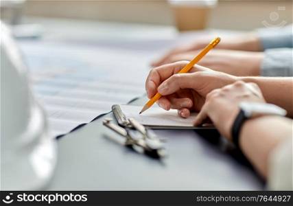 construction business, architecture and buiding concept - close up of architect with blueprint, notebook and pencil working at office. architect with notebook working at office