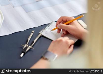 construction business, architecture and building concept - close up of architect with blueprint, notebook and pencil working at office. architect with notebook working at office
