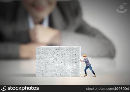 Construction concept. Businesswoman looking at man in hardhat pulling brick wall