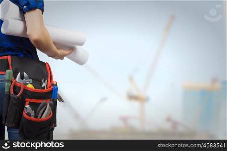 Construction concept. Close up of woman mechanic with yellow helmet in hand against city background
