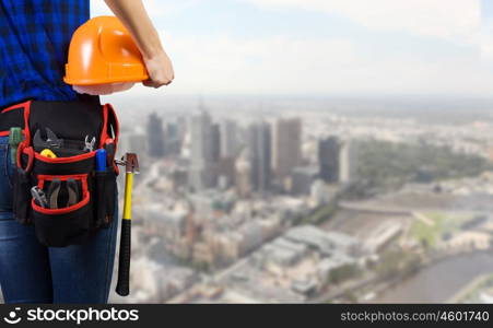 Construction concept. Close up of woman mechanic with yellow helmet in hand against city background