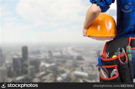 Construction concept. Close up of woman mechanic with yellow helmet in hand against city background