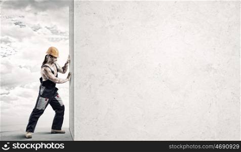 Construction concept. Strong man in uniform and helmet pushing wall