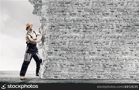 Construction concept. Strong man in uniform and helmet pushing wall