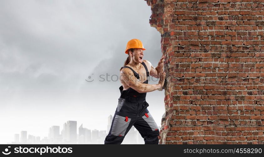 Construction concept. Strong man in uniform and helmet pushing wall. Place for text