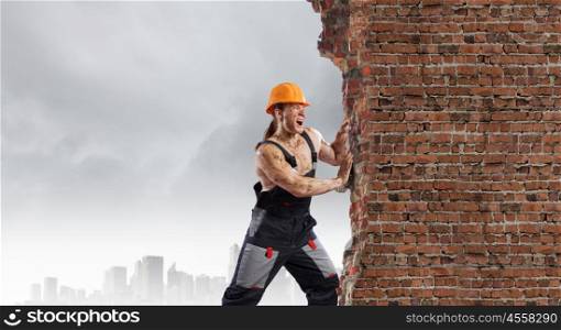 Construction concept. Strong man in uniform and helmet pushing wall. Place for text