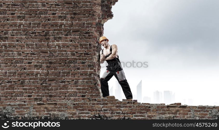 Construction concept. Strong man in uniform and helmet pushing wall. Place for text