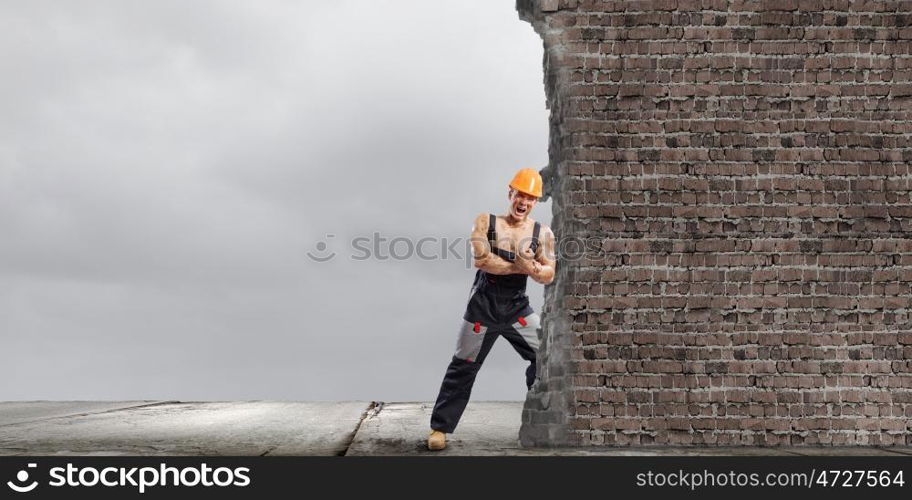 Construction concept. Strong man in uniform and helmet pushing wall. Place for text