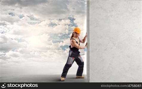 Construction concept. Strong man in uniform and helmet pushing wall. Place for text