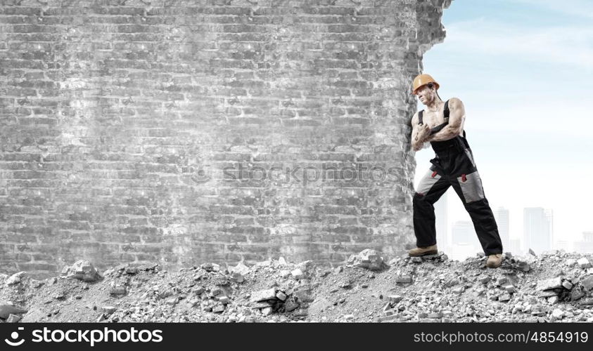 Construction concept. Strong man in uniform and helmet pushing wall. Place for text