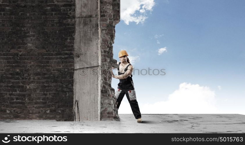 Construction concept. Strong man in uniform and helmet pushing wall. Place for text