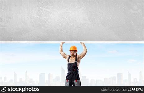 Construction concept. Strong man in uniform lifting wall above head