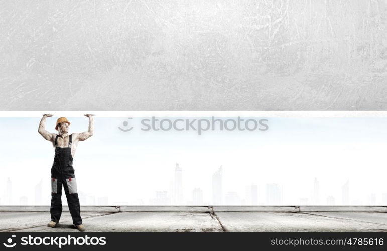 Construction concept. Strong man in uniform lifting wall above head