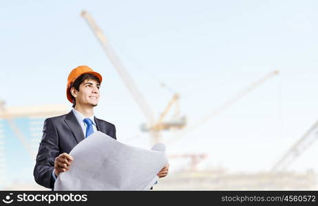 Construction concept. Young man engineer in helmet examining construction project