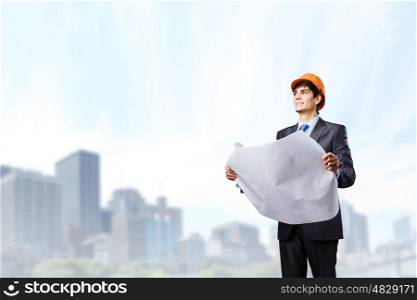 Construction concept. Young man engineer in helmet examining construction project