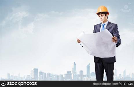 Construction concept. Young man engineer in helmet examining construction project