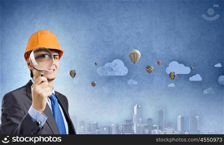 Construction concept. Young man engineer with magnifier against city background