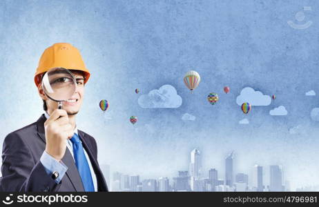 Construction concept. Young man engineer with magnifier against city background