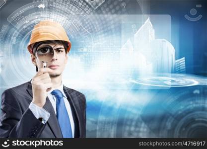 Construction concept. Young man engineer with magnifier against construction media model