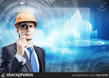 Construction concept. Young man engineer with magnifier against construction media model