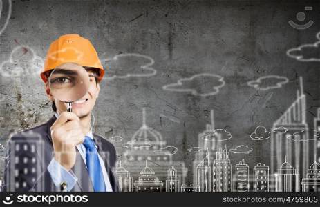 Construction concept. Young man engineer with magnifier against sketch background