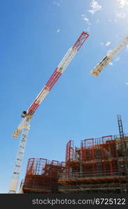 Construction cranes and scaffolding building under construction against blue sky