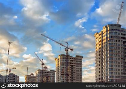 Construction cranes and tops of new residential high-rise buildings against the blue sky with clouds on a summer day. Moscow Region, Russia - June 2017.. Construction Of A New Microdistrict