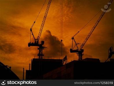 Construction cranes on high-rise building with dramatic orange sky and clouds at sunset time in the evening. Construction site of commercial building or condominium in city. Architecture background.
