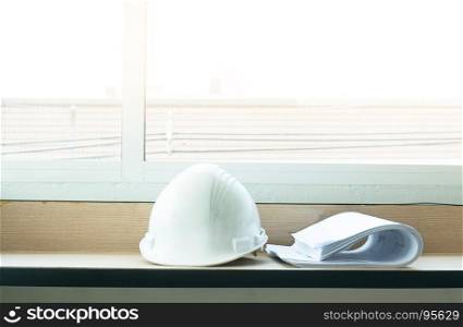 Construction drawing blueprints and white hard hat on table