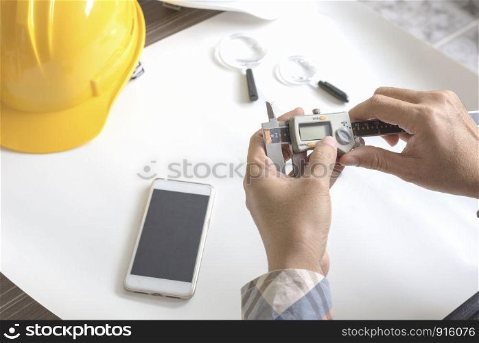 Construction engineer measuring with vernier caliper. Business and Technology concept. Safety helmet and Drawing paper elements. Civil and Drawing sketch theme. Smart phone element