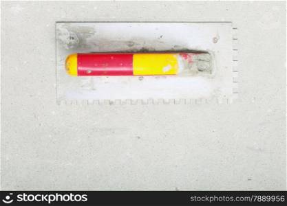 construction equipment dirty red yellow trowel used for masonry on rough unfinished concrete surface with copy space