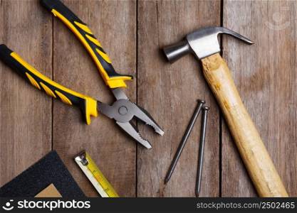 Construction instruments on wooden table - sandpaper, pliers, measuring tape, hammer, nails