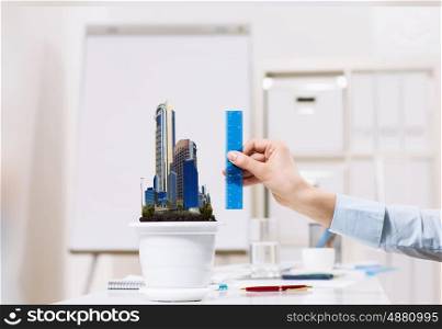 Construction investment. Close up of male hand measuring with ruler model of city