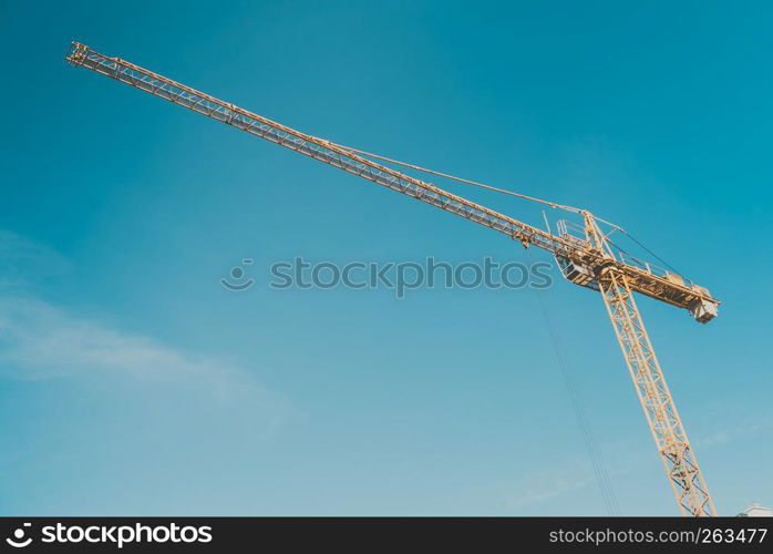 Construction site building hoisting crane on evening clear blue sky background. Industrial object concept.. Crane against blue sky.