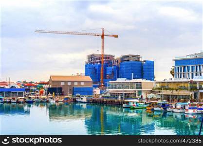 Construction site by Limassol waterfront, boats moored in marina with cafes and restaurants, Cyprus