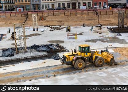Construction site in the middle of the old european city. Bulldozer works with sand pile in downtown, building engineering