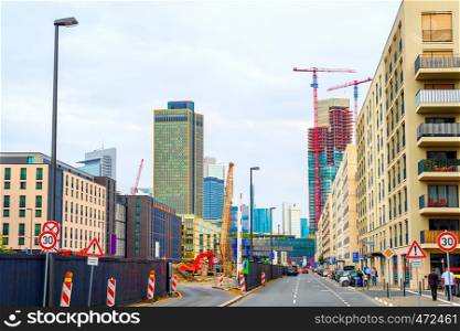 Construction site on urban street of Frankfurt downtown, city skyline with moder architecture, cars parked by road, Germany