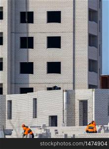 Construction site. Unfinished apartment building. Construction workers dressed in special clothing laying bricks.