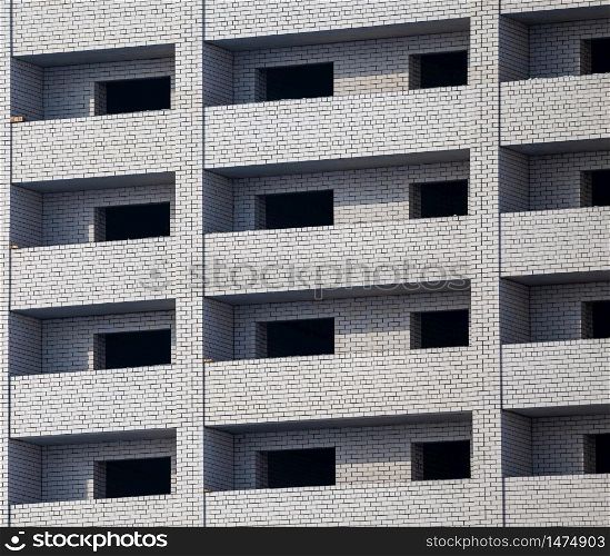 Construction site. Unfinished apartment building made of white bricks. Empty windows and balconies.